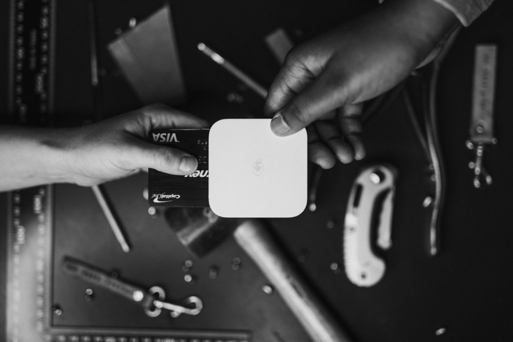 two hands, one putting a credit card in a square reader.